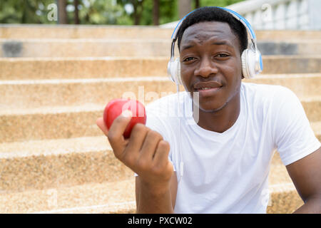 Homme africain à l'écoute de la musique avec des écouteurs et holding Red Apple Banque D'Images