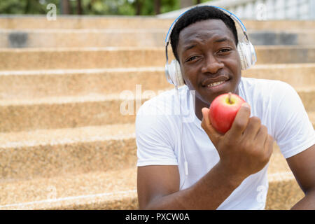 Homme africain à l'écoute de la musique avec des écouteurs et holding Red Apple Banque D'Images