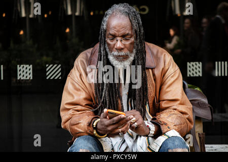 Un homme dreadlocked regarde son smartphone Blackberry Banque D'Images