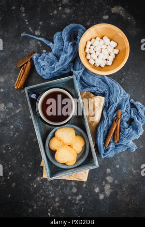 Émaillé bleu tasse de thé, des bâtons de cannelle, d'anis étoile et des sablés sur un fond sombre. Vue d'en haut. Banque D'Images