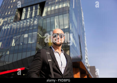 Bel homme élégant avec des lunettes de soleil en face de l'immeuble de bureaux Banque D'Images