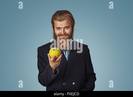 Hipster barbu businessman holding donnant tenant une pomme verte dans sa main isolé sur fond bleu. La face positive d'expression, l'émotion humaine, bod Banque D'Images