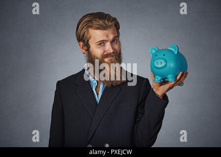 Portrait of young businessman hipster barbu man holding a piggy bank contre un mur à l'arrière-plan gris grunge studio. Visage neutre d'expression, les droits de l'em Banque D'Images