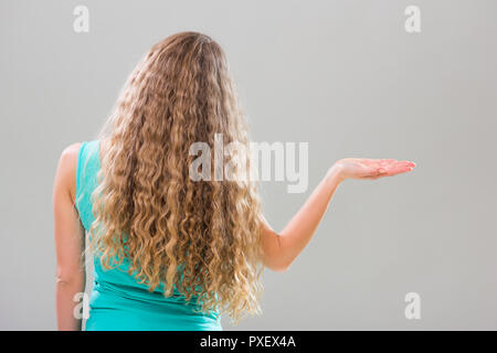 Femme avec de longs cheveux blonds magnifiques gestes sur fond gris. Banque D'Images
