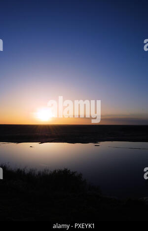 Coucher du soleil sur le lac serein à Meredith Lake, Texas, USA, avec un ciel bleu et orange contrastant sur le territoire lointain noir, et les ombres de l'herbe Banque D'Images