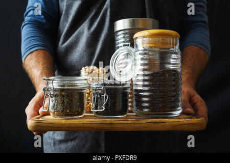 Mettre les céréales et les graines dans des bocaux en verre en mains l'homme. L'alimentation saine Banque D'Images