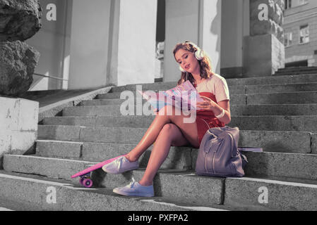 Fille assise sur l'escalier extérieur de la lecture de magazine de mode et d'écouter de la musique Banque D'Images