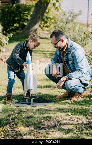 Heureux père et fils jouant avec fusée modèle ensemble à jour ensoleillé Banque D'Images