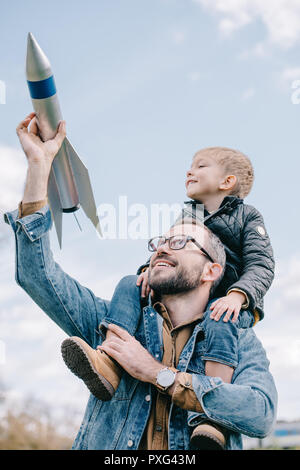 Heureux père exerçant son petit fils sur le cou et spéléologie maquette de fusée contre sky Banque D'Images