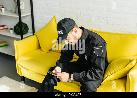 Beau jeune policier avec smartphone assis sur table jaune Banque D'Images