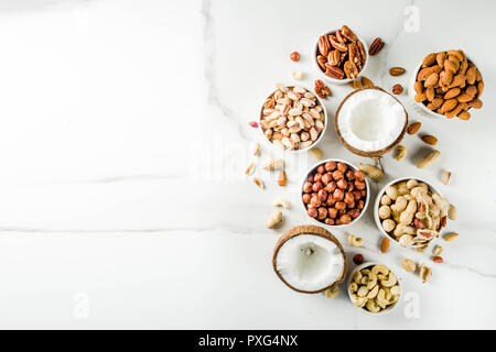 Différents types de noix - noix, pacanes, arachides, noisettes, noix de coco, amandes, noix de cajou, dans des bols, sur une table de marbre blanc Vue de dessus Banque D'Images