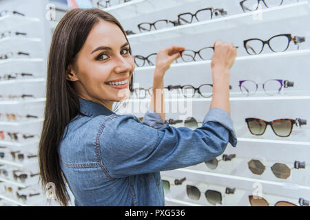 Portrait of smiling young woman taking lunettes des tablettes et à la recherche en ophtalmologie de l'appareil photo au shop Banque D'Images