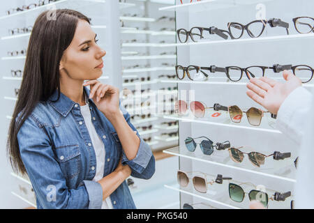 Thoughtful woman looking at ouvrages tout en pointant à la main d'oculiste à lunettes pour sa à optica Banque D'Images