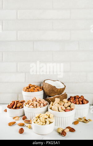 Différents types de noix - noix, pacanes, arachides, noisettes, noix de coco, amandes, noix de cajou, dans des bols, sur une table de marbre blanc Vue de dessus Banque D'Images