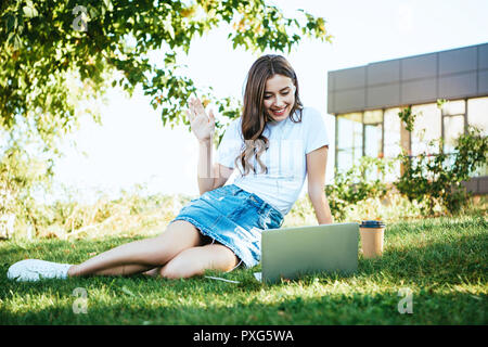 Belle jeune fille prenant part à webinaire et agitant la main lors de conférence vidéo Banque D'Images