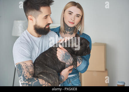 Homme barbu tenant bouledogue français et belle girl looking at camera in new house Banque D'Images