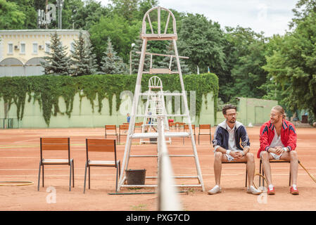 Raquettes en bois avec des amis sportifs assis sur des chaises sur court de tennis Banque D'Images