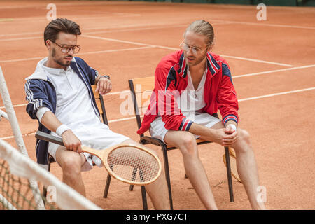 Raquettes en bois avec des amis sportifs assis sur des chaises après la formation sur court de tennis Banque D'Images