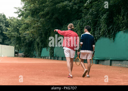 Vue arrière de style rétro avec des raquettes en bois d'amis marche sur court de tennis Banque D'Images