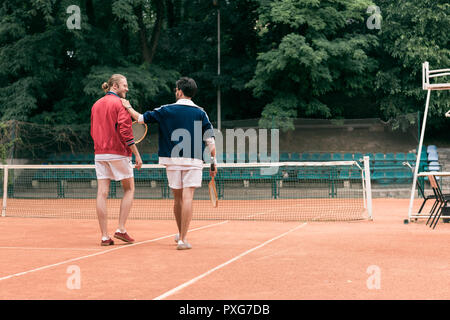 Vue arrière de vieux amis avec raquettes en bois sur pied court de tennis Banque D'Images