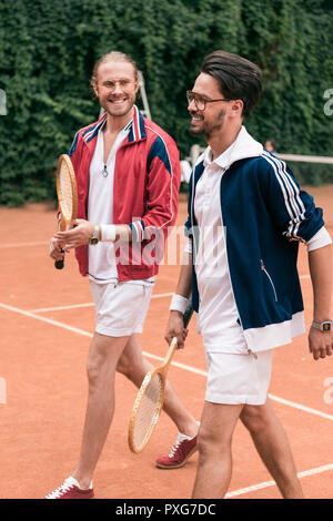 Amis de style rétro souriant avec des raquettes en bois sur pied court de tennis Banque D'Images