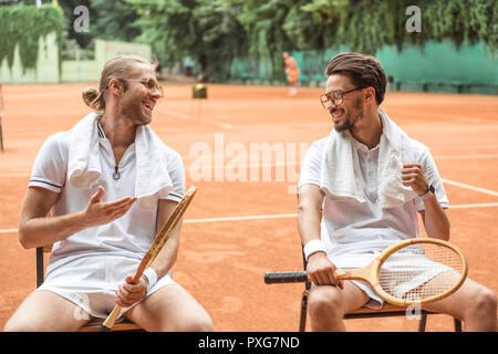 Sourire les joueurs de tennis avec des serviettes et des chaises en bois reposant sur des raquettes Banque D'Images