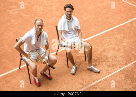 Les joueurs de tennis avec des raquettes en bois vintage reposant sur des chaises Banque D'Images