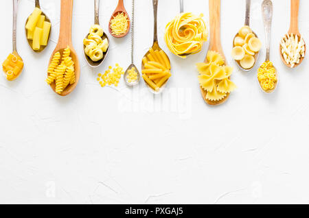 Variété de types et formes de pâtes italiennes dans des cuillères en bois sur fond blanc à partir de ci-dessus. La cuisine italienne food Concept et design de menu. Les pâtes sèches Banque D'Images