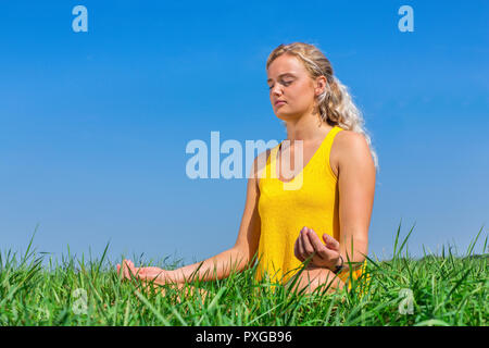 Jeune blonde hollandaise méditant dans la nature avec ciel bleu Banque D'Images