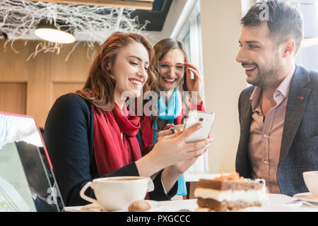 Trois jeunes amis en utilisant un téléphone mobile pour le plaisir pendant une pause-café Banque D'Images