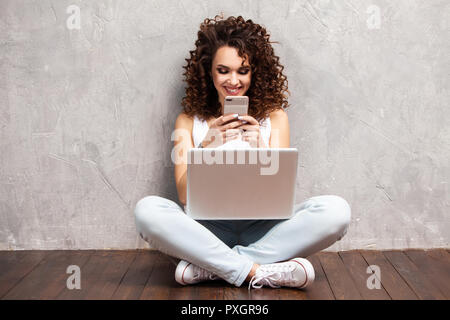 Jeune femme assise sur le sol avec les jambes croisées et l'utilisation de l'ordinateur portable sur fond gris Banque D'Images