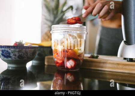 Femme préparant des jus à partir d'ingrédients frais dans la cuisine. Les décisions un smoothie le matin. L'ajout de fruits coupés dans blender. Banque D'Images