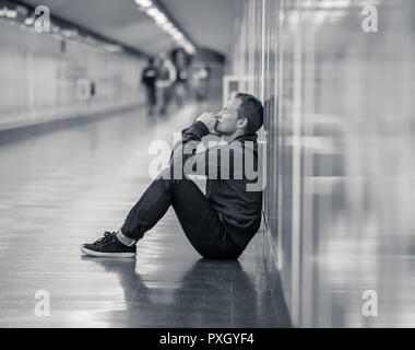 Sans emploi misérable jeune homme pleurer toxicomane sans domicile dans la dépression Le stress assis sur le sol du tunnel du métro de la rue à la recherche désespérément leaning on wall Banque D'Images