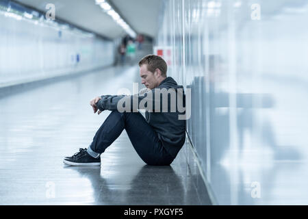 Sans emploi misérable jeune homme pleurer toxicomane sans domicile dans la dépression Le stress assis sur le sol du tunnel du métro de la rue à la recherche désespérément leaning on wall Banque D'Images