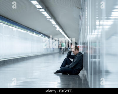 Sans emploi misérable jeune homme pleurer toxicomane sans domicile dans la dépression Le stress assis sur le sol du tunnel du métro de la rue à la recherche désespérément leaning on wall Banque D'Images