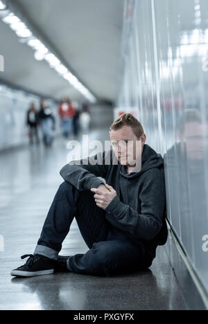 Sans emploi misérable jeune homme pleurer toxicomane sans domicile dans la dépression Le stress assis sur le sol du tunnel du métro de la rue à la recherche désespérément leaning on wall Banque D'Images