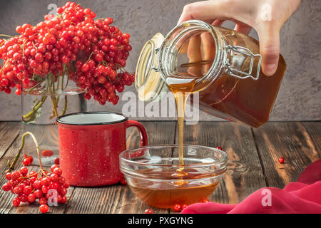 Les baies d'une vie encore viburnum dans un verre et tasse de thé chaud et le miel sur une table en bois. Part verse le miel dans un bol. Concept d'automne alimentation l'agriculture, Banque D'Images