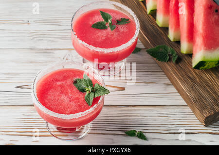 Boire des smoothies de pastèque rouge plats en verre décoré de feuilles de menthe et le sucre blanc morceaux de fruits sur une planche à découper le tableau blanc concept de guérir Banque D'Images