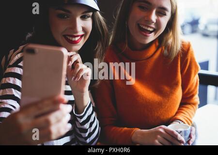 Deux jeunes femmes assises dans un café, de boire leur café le matin et surfer sur le net sur les téléphones intelligents. Banque D'Images