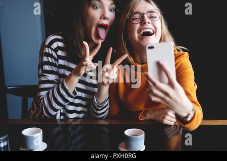 Deux jeunes femmes assises dans un café, de boire leur café le matin et surfer sur le net sur les téléphones intelligents. Banque D'Images