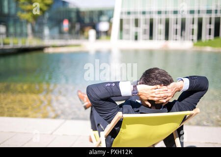 Jeune homme d'apprécier sa pause sur une chaise longue en face de l'office de tourisme journée Banque D'Images