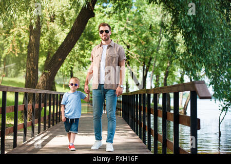 Père et fils en lunettes holding hands on bridge at park Banque D'Images