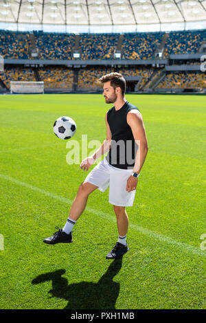 Séduisant jeune joueur de foot balle rebondissante sur jambe à stade Banque D'Images
