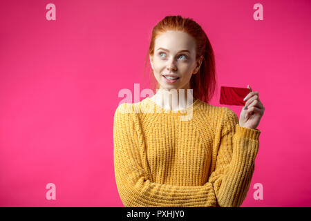 Gingembre Happy woman holding credit card isolé sur fond rose. Banque D'Images