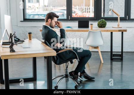 Vue de côté assez businessman sitting on chair et toucher du nez in office Banque D'Images