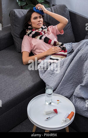 Portrait de jeune femme malade avec une température élevée holding paquet de glace sur la tête en position couchée sur la table Banque D'Images