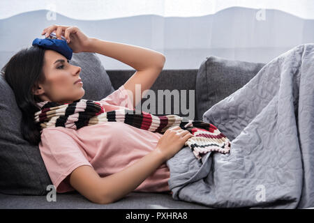 Jeune femme malade avec une température élevée holding paquet de glace sur la tête en position couchée sur la table Banque D'Images