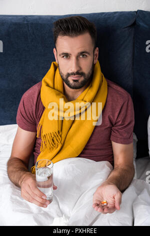 Portrait d'un jeune homme assis au lit avec un verre d'eau et de comprimés Banque D'Images