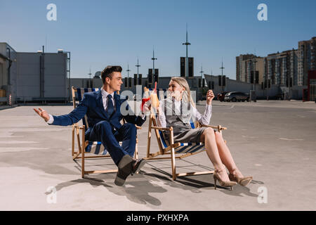 Les jeunes gens d'affaires se détendre sur les chaises longues clinking glasses avec des cocktails sur le stationnement Banque D'Images