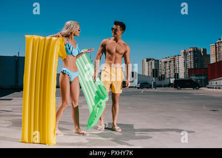 Attractive young couple en vêtements de plage avec lits gonflables sur le stationnement Banque D'Images